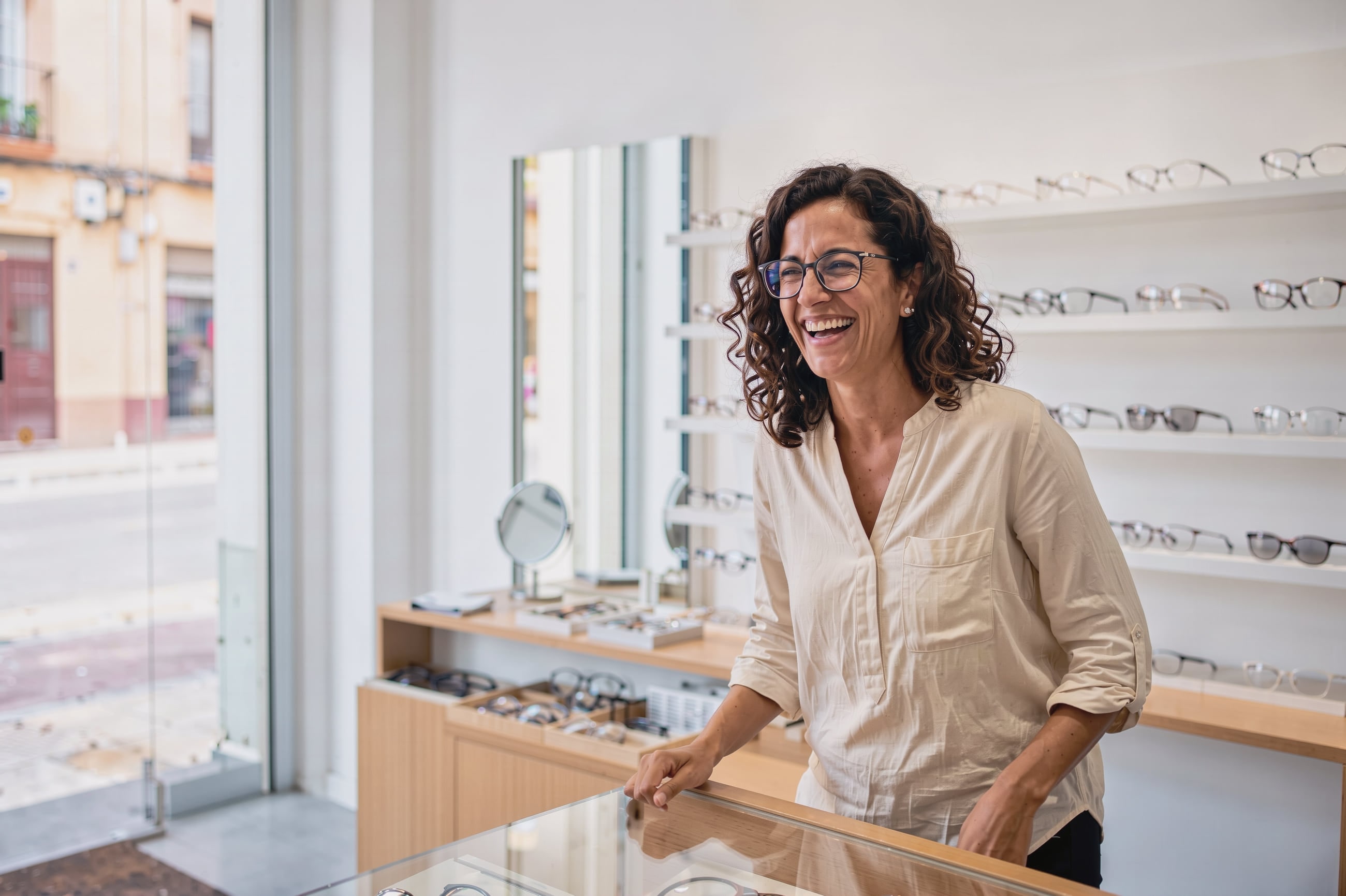 Clienta con gafas graduadas riendo en una óptica luminosa